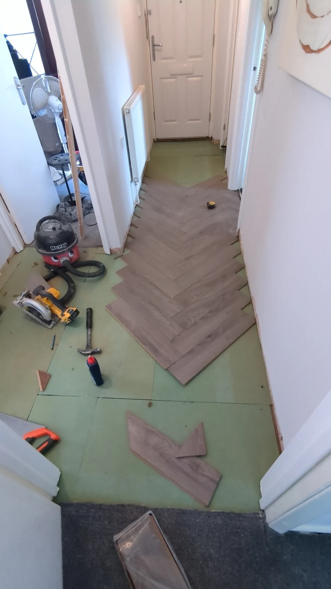 Herringbone laminate being laid over green fibreboard underlay in a hallway, with skirtings removed