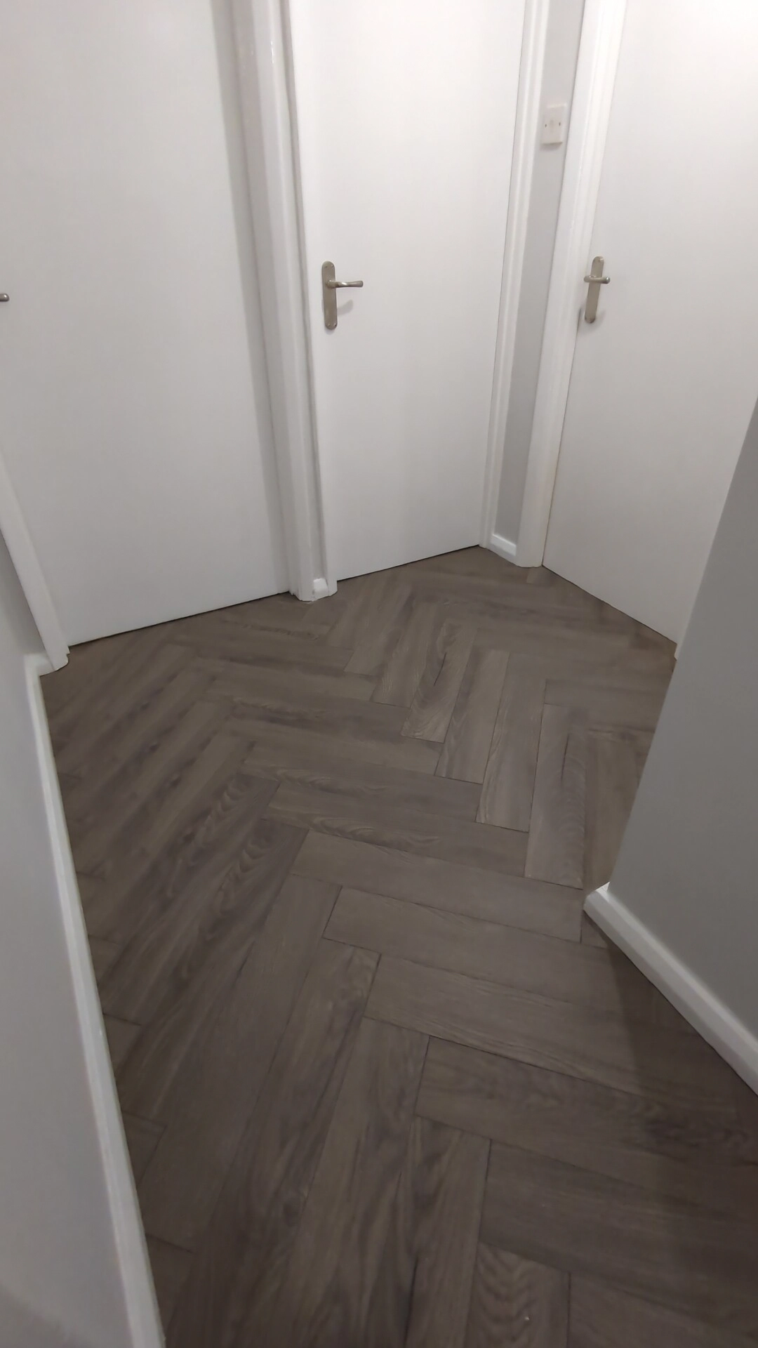 Herringbone laminate flooring running beneath undercut door linings with no trim or beading