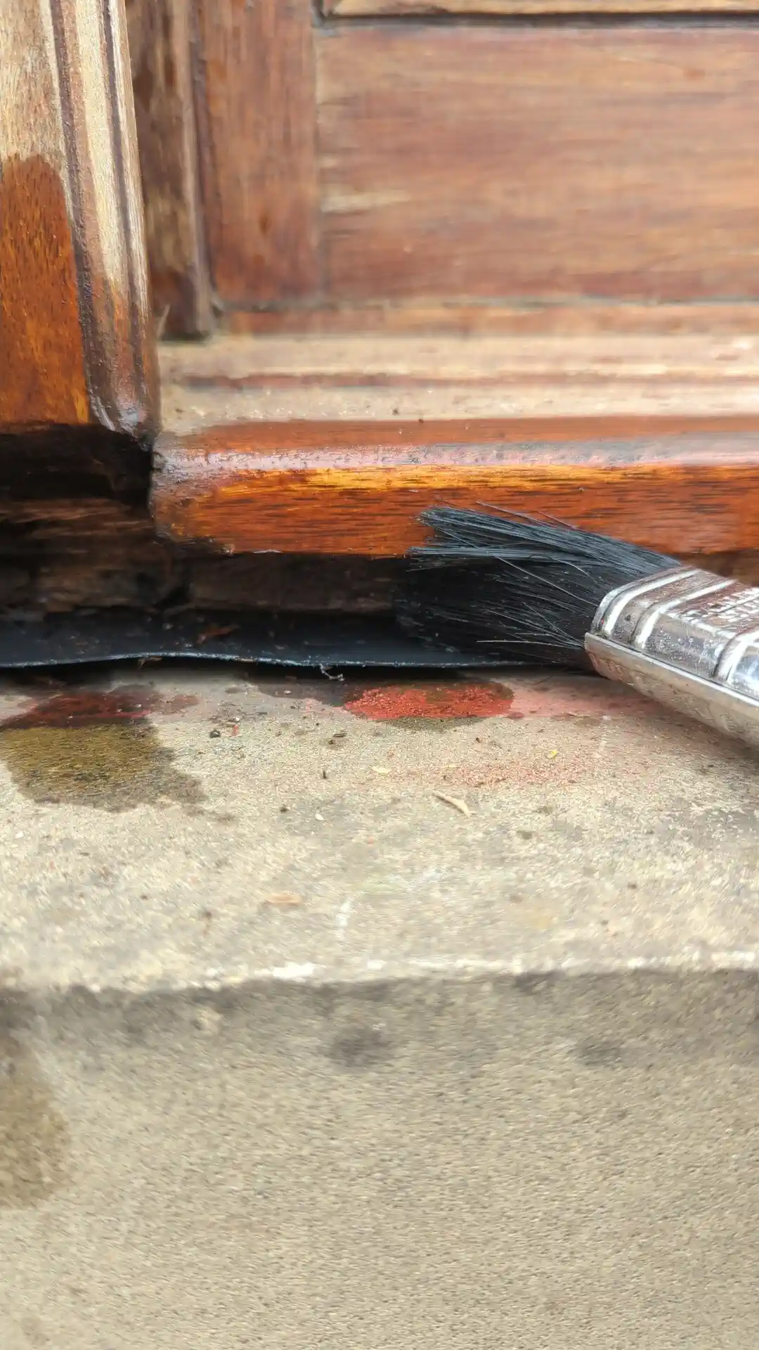 Wood preserver being brushed into a bare timber window sill corner before repair