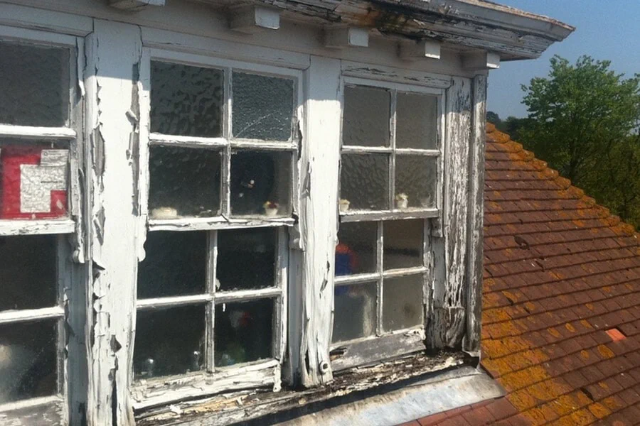 Timber sash windows with paint flaking away and eroded, decayed frames and sills — past economical repair